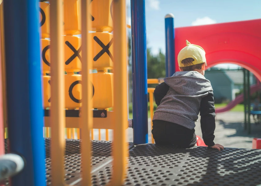 jeune enfant assis de dos dans une structure de jeux